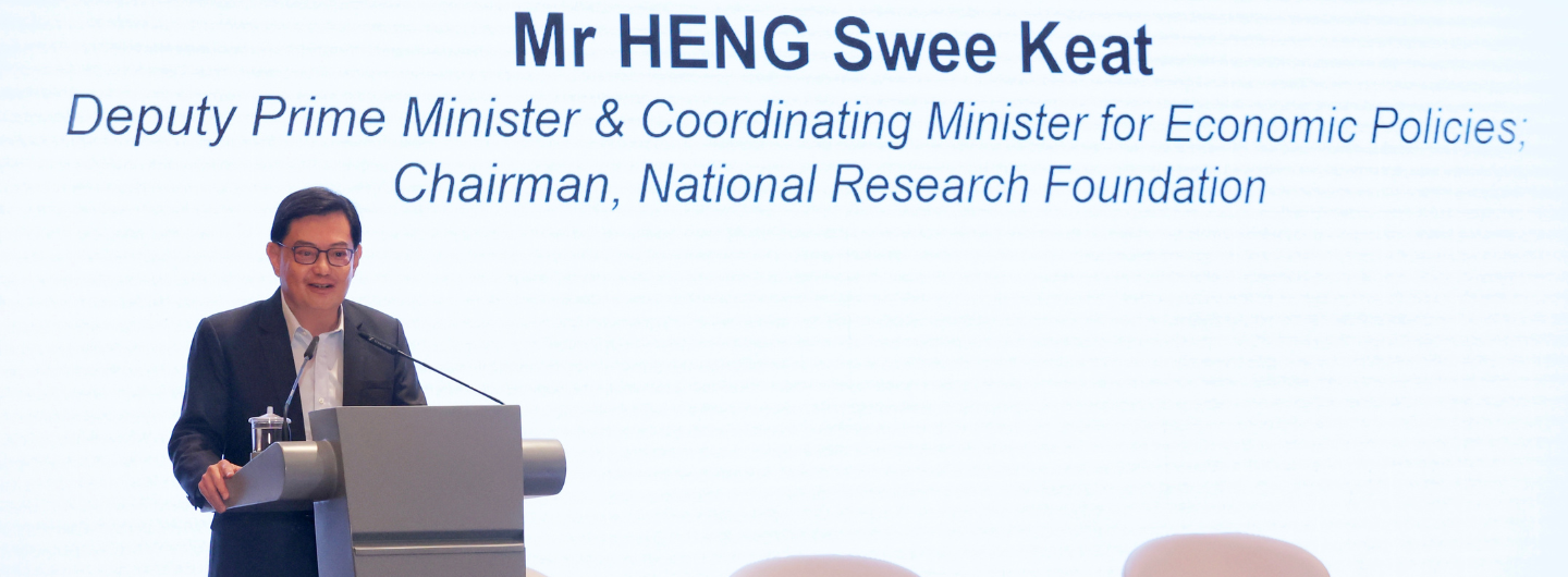 Man at podium, Mr HENG Swee Keat, microphone, water glass, text above.